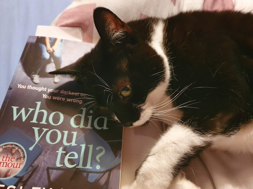 The book Who Did You Tell? being used as a pillow by a black and white cat